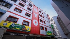 Un hotel con una facciata rossa e bianca ben visibile, numerose finestre e insegna per un ristorante chiamato "RK Banana Leaf" al piano terra.