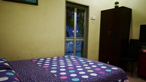 Una camera da letto con un letto coperto da una coperta a pois, un armadio, una televisione e una finestra con vista su palme.