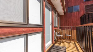 Un balcone con pavimento in legno, un tavolino con sedie e una ringhiera in metallo.
