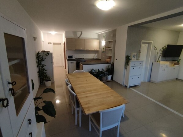 A modern kitchen with white cabinets, a wooden dining table, and potted plants.