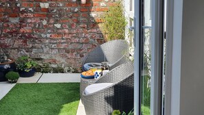 Un área de estar exterior con muebles de mimbre y una mesa dispuesta para el desayuno, incluyendo croissants y una cafetera.