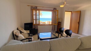 Un soggiorno con divano, poltrone, televisore e vista sull'oceano.