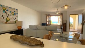 Un soggiorno con un divano, un tavolo da pranzo con sedie, un quadro appeso e vista mare attraverso una finestra.