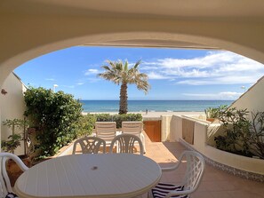 A patio with a round table and chairs, a palm tree, and a view of the sea. - Ample duplex frontline to the Med (La Manga del Mar Menor)
