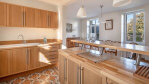 A modern kitchen with wooden cabinets, a large island, pendant lights, and a view of the outdoors.