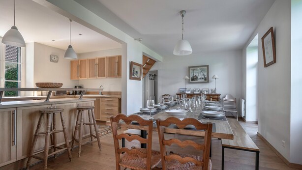 A spacious kitchen with wooden cabinets, a large island with stools, and a dining area with a long table set for six.