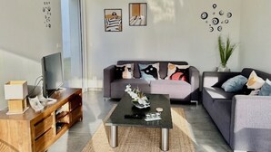 A modern living room with a sofa, coffee table, TV, and decorative items. - Villa Rubis, an ecological house with modern comfort (Varengeville-sur-Mer)