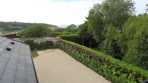 A residential property with a paved driveway, a well-maintained hedge, and a view of a green landscape with trees and hills in the distance. - Villa Rubis, an ecological house with modern comfort (Varengeville-sur-Mer)