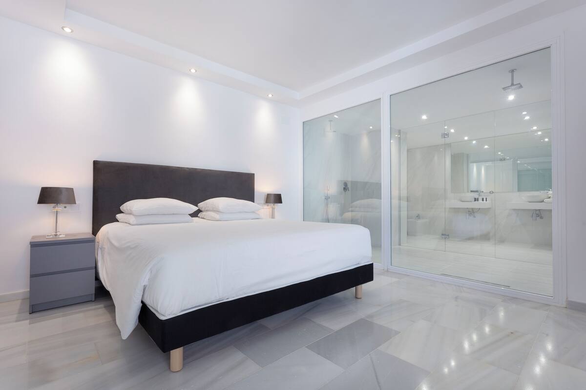 Un dormitorio moderno con una cama grande, mesitas de noche y un box de ducha de vidrio.