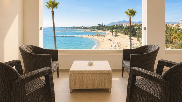 A balcony with wicker furniture, a small table, and a view of a beach and cityscape. - B51 Executive Flats Marbella Puerto Banus (Marbella)
