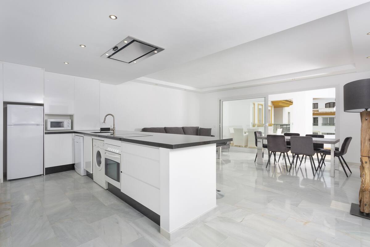 Una cocina moderna con armarios blancos, una isla central y electrodomésticos integrados.