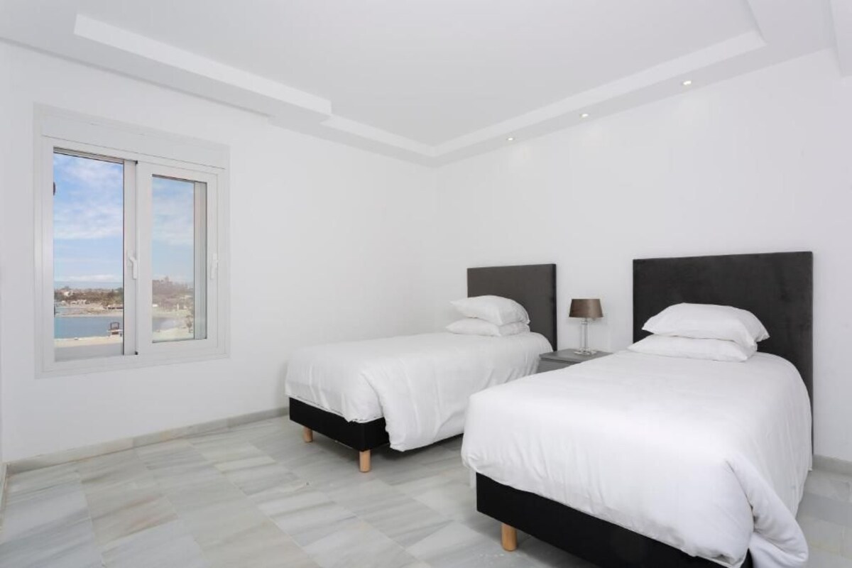 A bedroom with two beds, a window with a view, and a ceiling light.