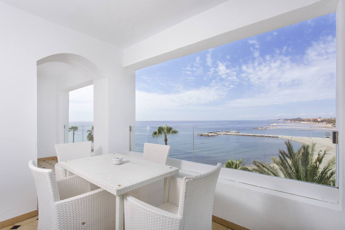 Un conjunto de comedor de mimbre blanco con vistas al mar y una costa lejana.
