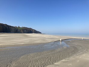 A beach with a clear sky, a sandy shore, and a cliff with a building on top.