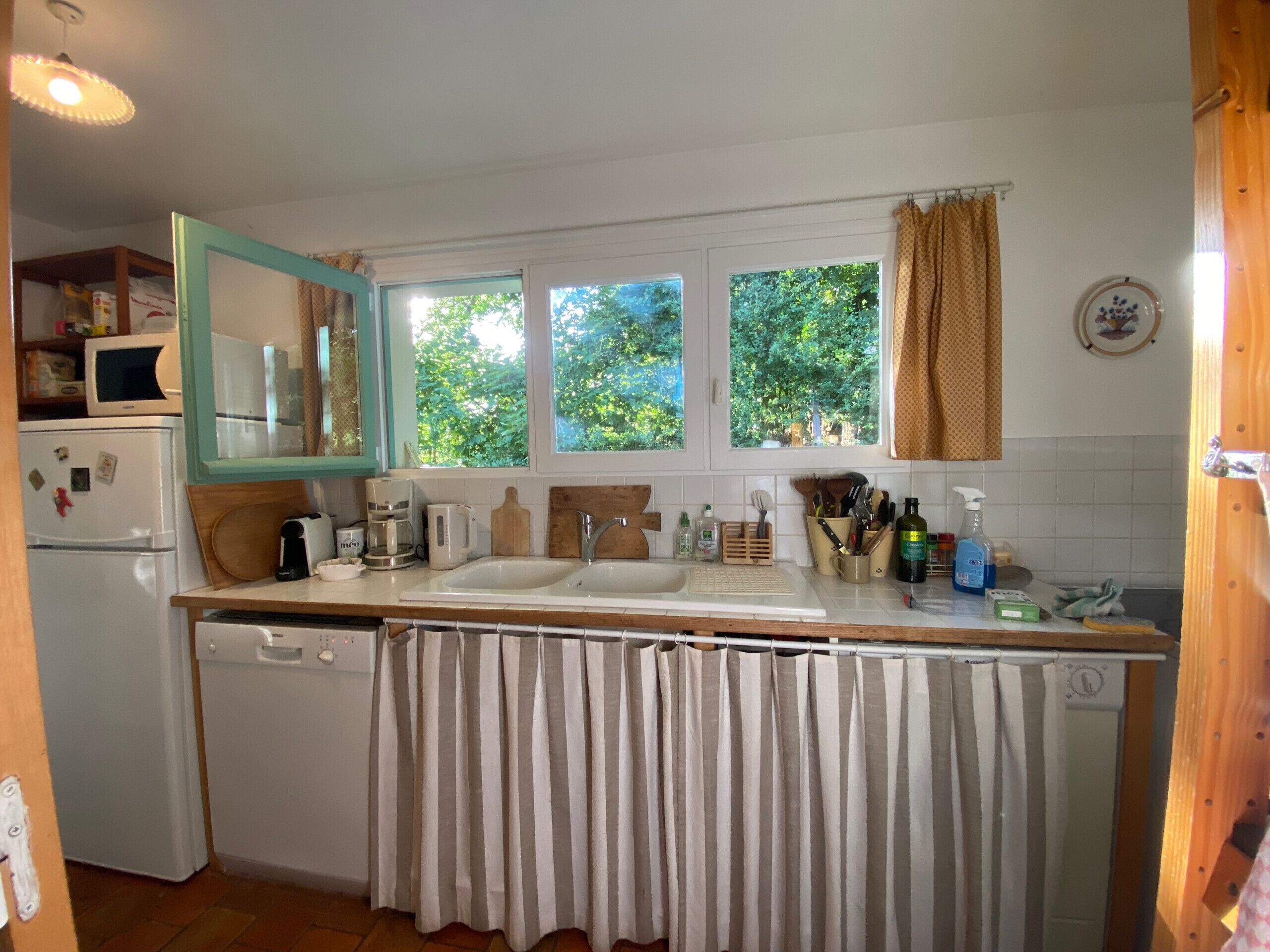 Una cocina con dos fregaderos, un refrigerador, un microondas y una ventana con cortinas.