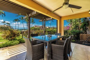 Eine Terrasse im Freien mit einem Tisch aus Glas, Korbstühlen und einem Deckenventilator.