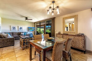 A spacious living area with a glass-top dining table, wicker chairs, a sofa, and a ceiling fan.