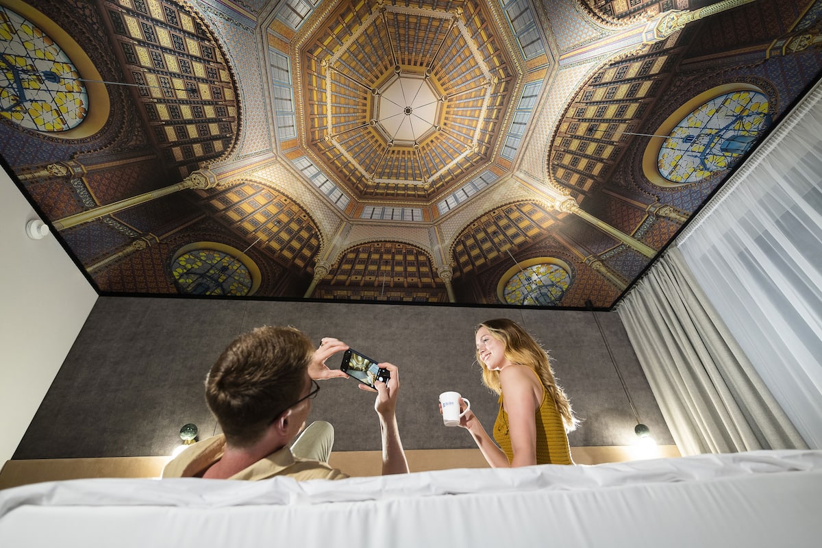 Une pièce dotée d’un grand plafond richement décoré et d’un lit recouvert de draps blancs.
