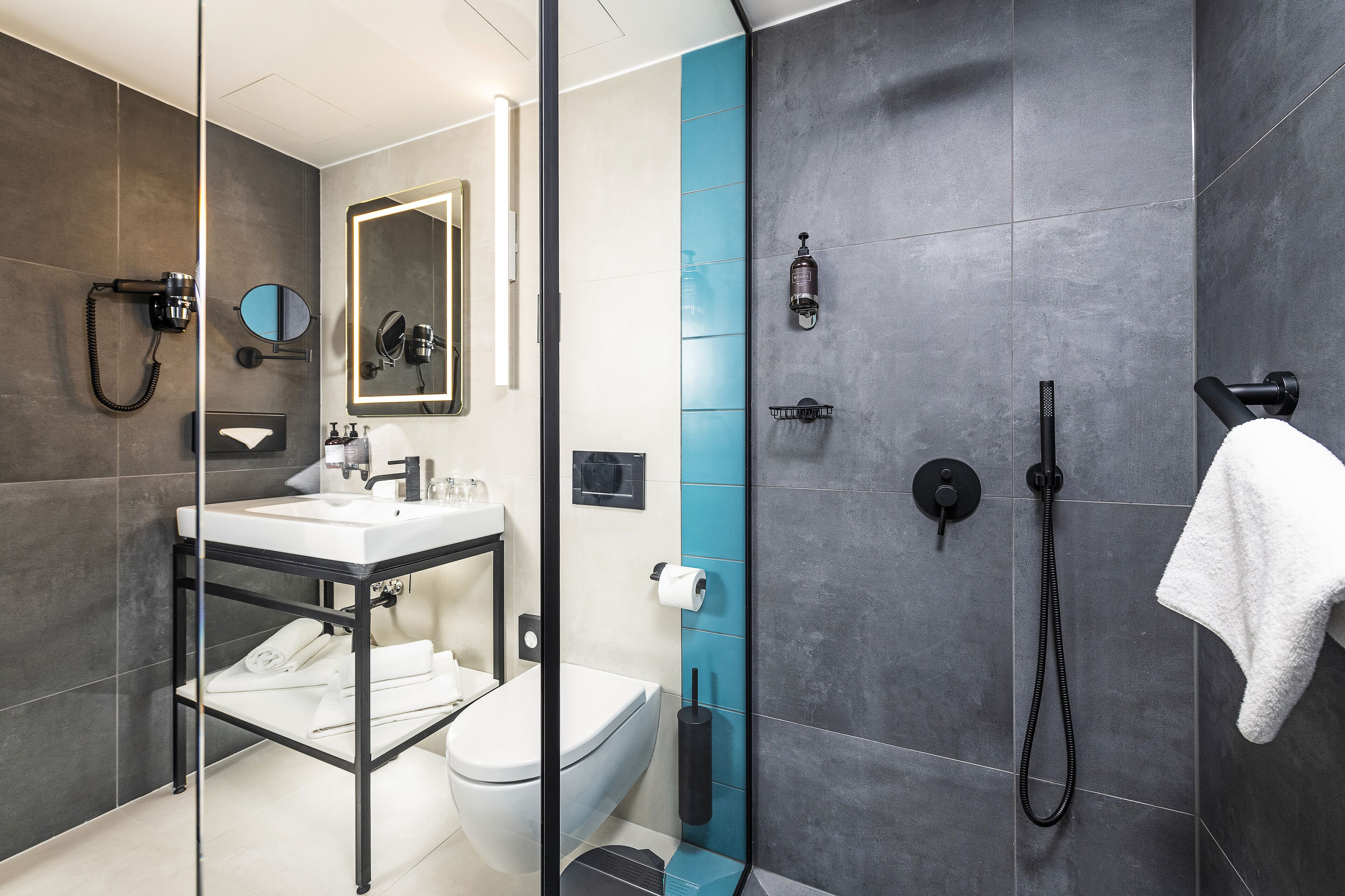 A modern bathroom with a glass shower enclosure, a white sink, and a black towel rack.