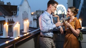 A couple on a balcony with lit candles, a Ferris wheel in the background, and a cityscape. - Three Corners Downtown Hotel (Budapest)