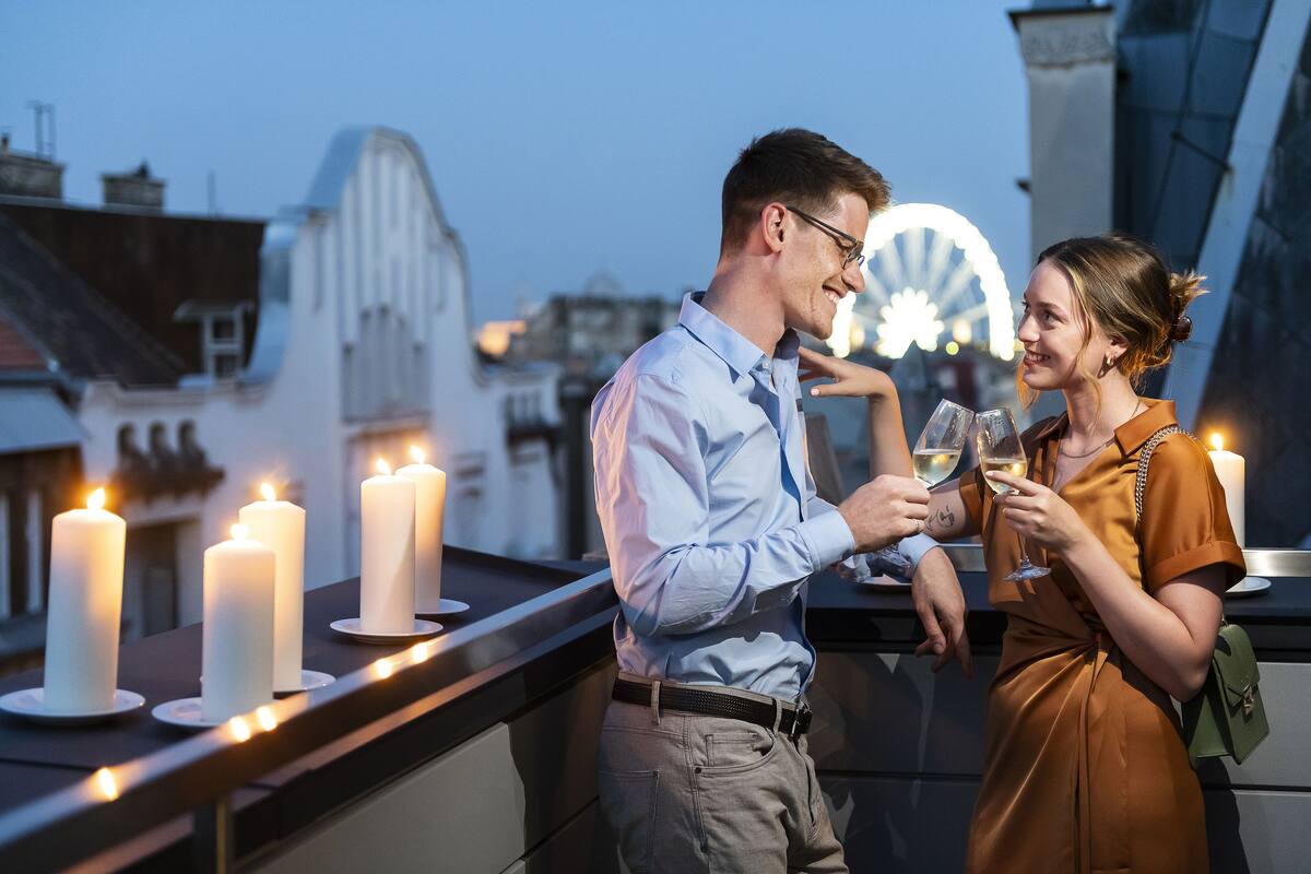 Un couple sur un balcon, des bougies allumées, une grande roue en arrière-plan et une vue sur la ville.