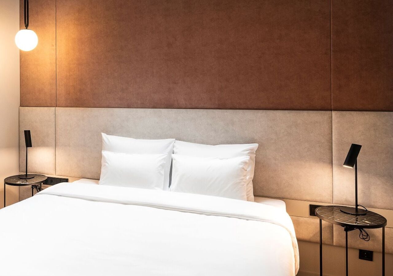 A modern hotel room with a large bed, two bedside tables, and a wall-mounted light fixture.