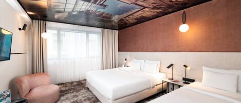 Habitación de hotel con una cama grande, una cama más pequeña, un área de descanso y un mural en el techo.