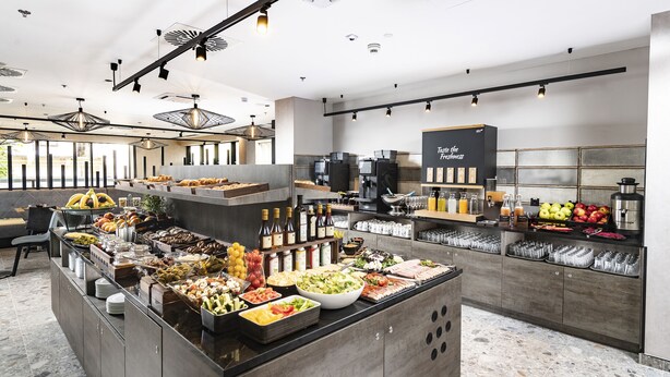 A modern buffet setup with various food items and beverages, including fruits, salads, and hot dishes. - Three Corners Downtown Hotel (Budapest)
