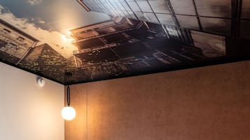 A room with a textured wall, a hanging light fixture, and a ceiling mural depicting a cityscape.