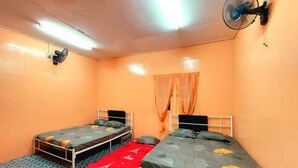 A room with two beds, a standing fan, and a window with curtains.