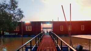 Un muelle de madera que lleva a un edificio con entrada de vidrio, rodeado de agua.