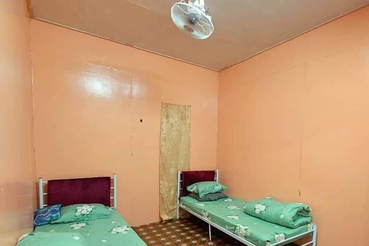 A small, single-room accommodation with two beds, a ceiling fan, and a patterned floor.