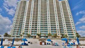 A tall hotel with multiple balconies, a beach area with sun loungers and umbrellas, and a clear sky. - 1BR 2BA @ THE AQUA SLEEPS 6!! (Panama City Beach)
