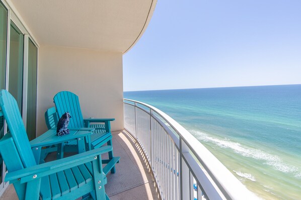 Un balcon avec des chaises turquoise et une table, donnant sur un océan d’un bleu limpide.