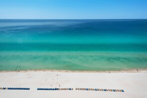A beach with clear turquoise water, a sandy shore, and rows of beach chairs.