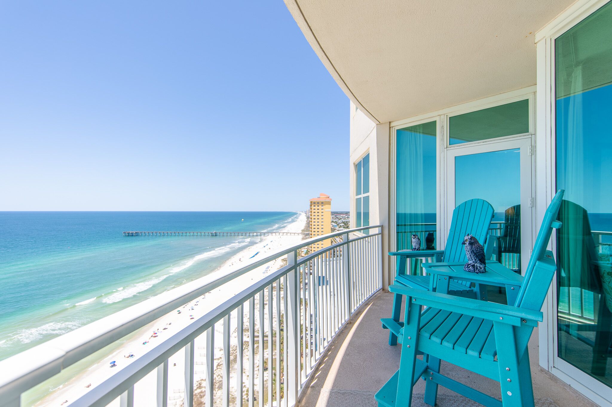 Een balkon met turquoise stoelen met uitzicht op een strand en de oceaan.