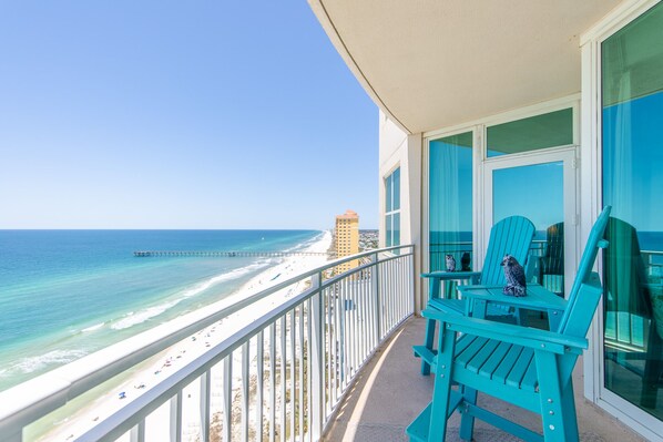 A balcony with turquoise chairs overlooking a beach and ocean.