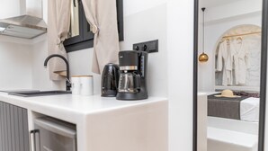 A modern hotel room with a white countertop, a coffee maker, a mirror, and a wardrobe with hanging robes.