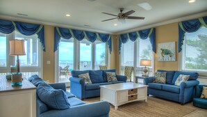 A spacious living room with a large window, a ceiling fan, and a view of the outdoors. - 7 Bed, 7.5 Bath, Oceanfront Home, Private Pool that can be heated (Garden City Beach)