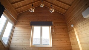 Un interior de madera con techo inclinado, tres lámparas colgantes esféricas y un amplio ventanal con vistas al exterior.