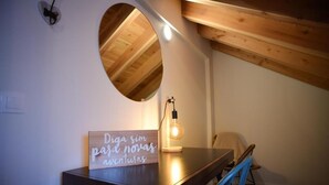 Una habitación con techo de madera, un espejo redondo, una mesa con un letrero y una silla.