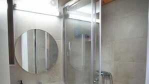 Un baño con ducha de vidrio, lavamanos pedestal y espejo.