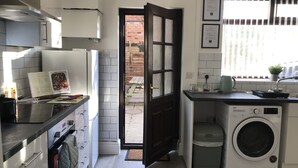 Une cuisine compacte équipée d’un lave-linge, un coin repas avec une table et des chaises, et une vue sur l’extérieur par une porte.