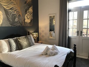 A neatly made bed with white linens and rolled towels, a dark wooden headboard, a wall-mounted lamp, and a window with curtains. - Stylish 3-bed Preston Home for Relaxing Comfy Stay (Preston)