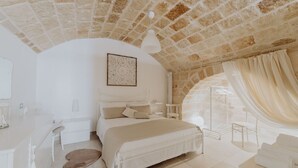 Un dormitorio con techo de piedra, una cama, una mesita de noche, una silla y una ventana con cortinas.