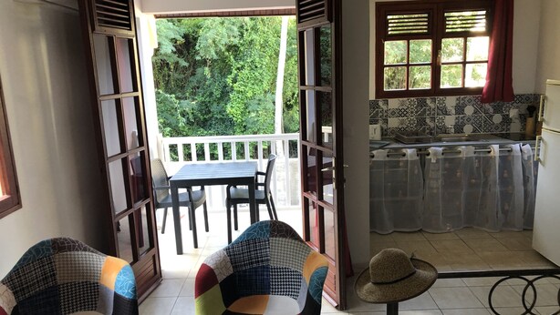 Et værelse med balkon, spisebord med stole, et tekøkken og en stol med mønster.