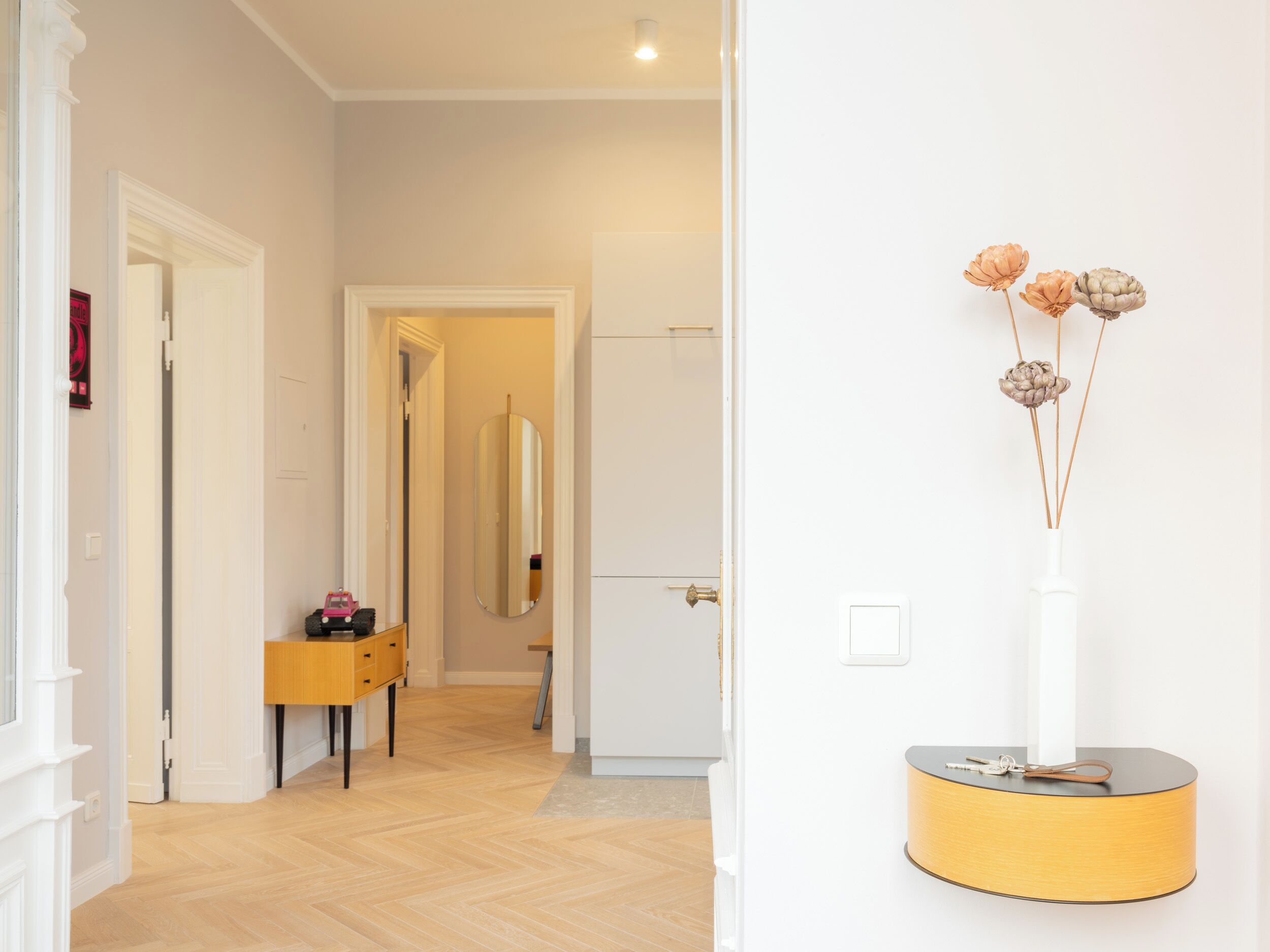 A hallway with a wooden floor, a small table with a toy car, a mirror, and a white door.