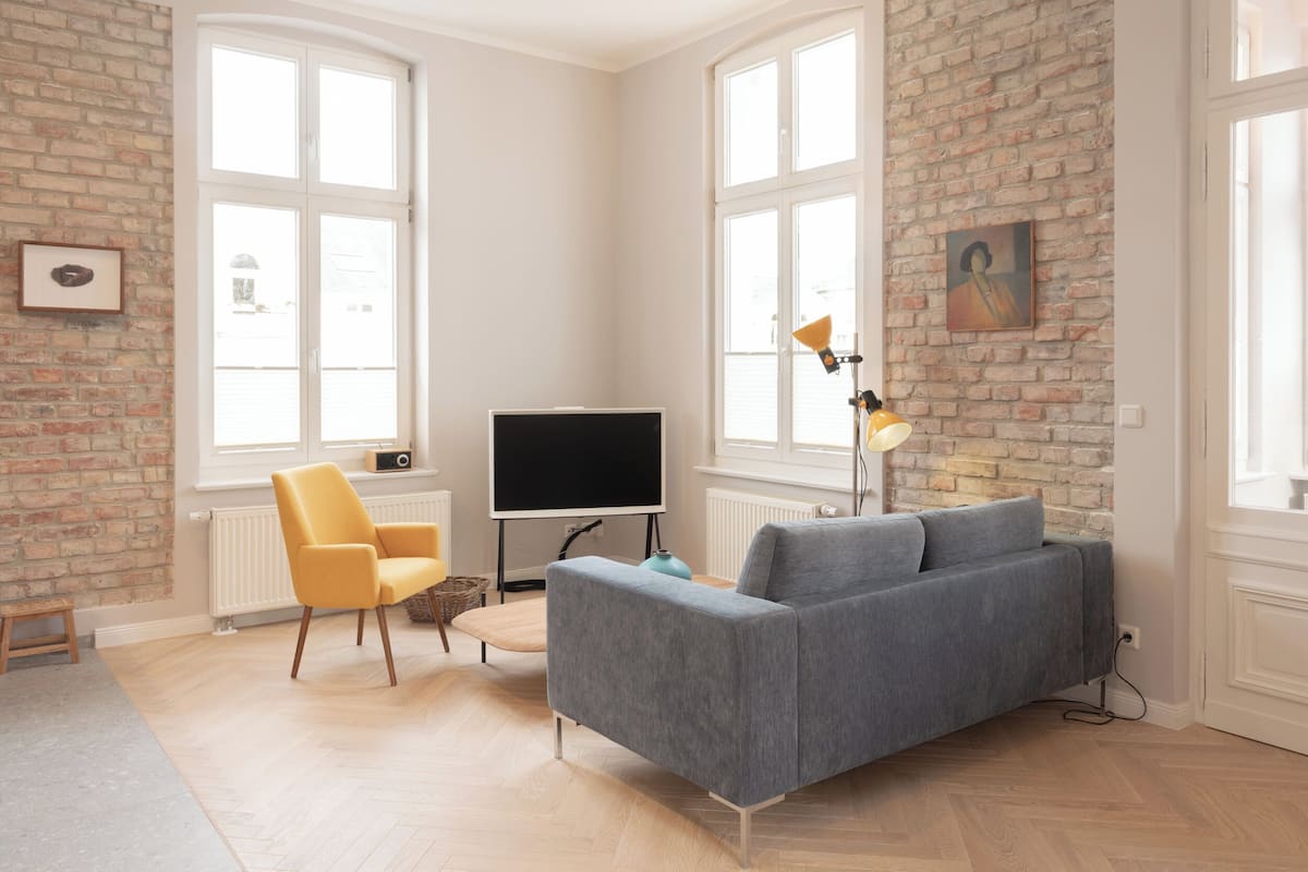 Una sala de estar moderna con un sofá gris, un sillón amarillo, un televisor de pantalla plana y una pared de ladrillo.