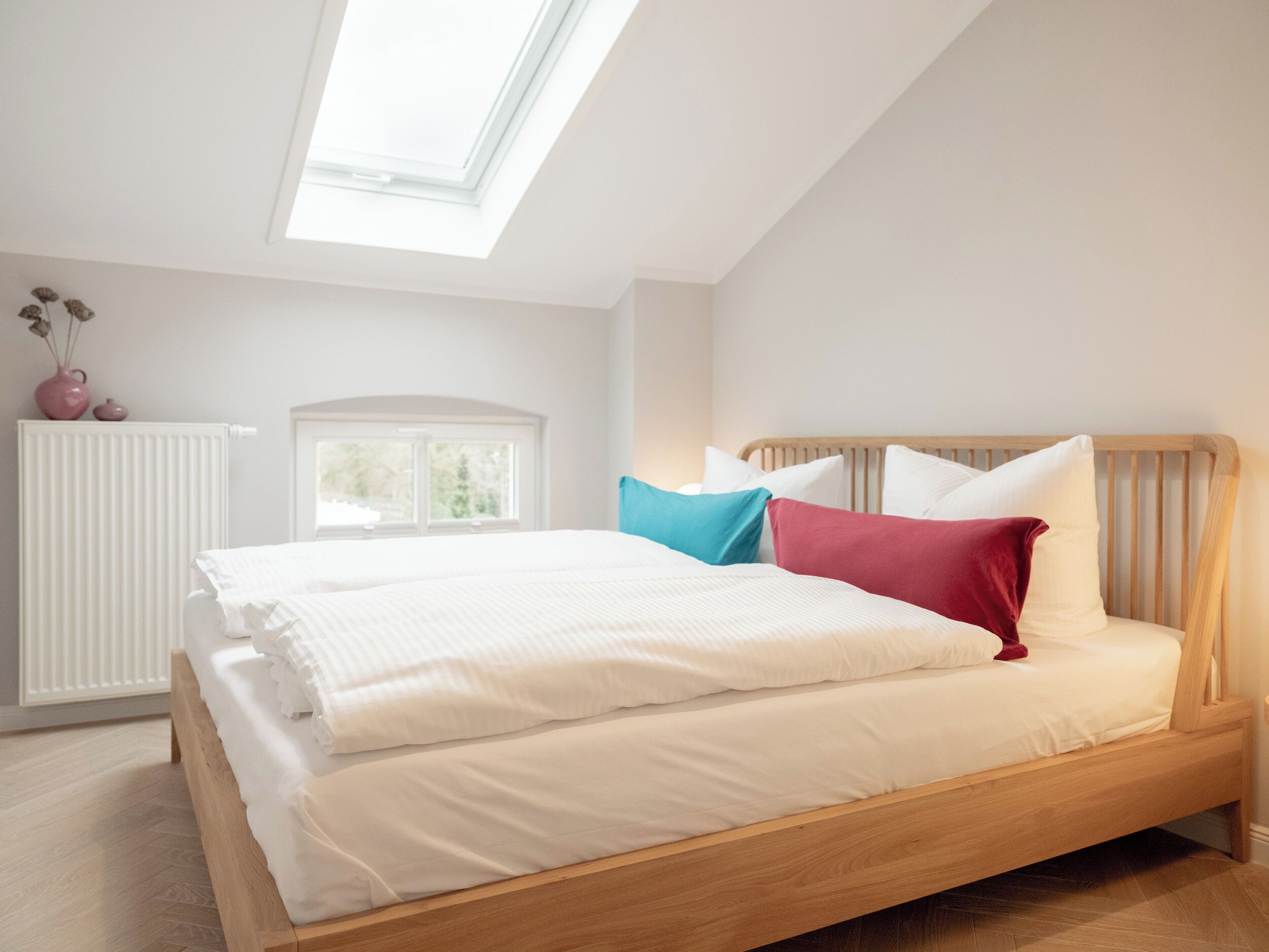 A bedroom with a skylight, a bed with white bedding, a wooden headboard, and a radiator.