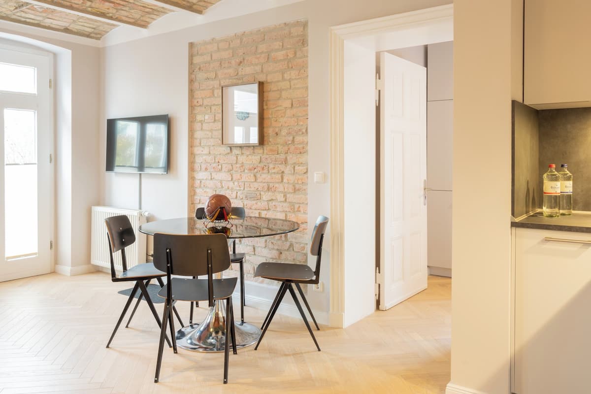 Un comedor moderno con una mesa redonda de vidrio, cuatro sillas negras y una pared decorada con ladrillos.